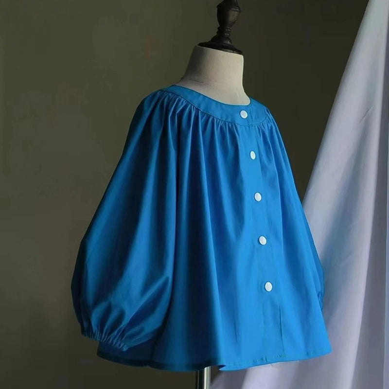 A mannequin models the Smocked Crewneck Raglan Sleeve Blouse by Longan Craft, featuring a bright blue loose fit and puffed sleeves. Download the free PDF sewing pattern to craft your own stylish blouse!.