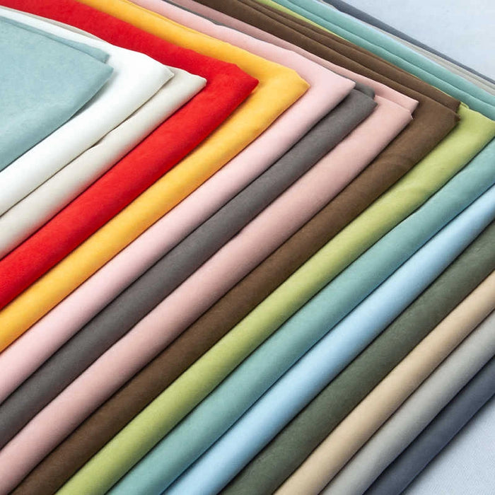 A diagonal stack of Longan Craft’s Solid Color Brushed Polyester Peachskin Fabric By The Yard in blue, green, yellow, red, brown, pink, and white—midweight microsuede with a velvety texture—ideal for dressmaking and apparel.