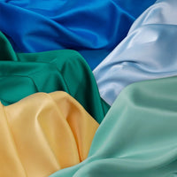 Longan Craft’s Solid Color Charmeuse Satin Fabric By The Yard features thick bridal satin with a smooth, silky texture in blue, green, yellow, and light blue—perfect for gowns and luxurious draped arrangements.