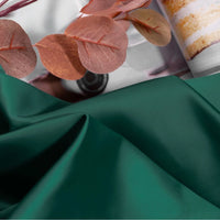 A close-up of Longan Craft’s Solid Color Charmeuse Satin Fabric By The Yard in green, featuring thick bridal satin texture with smooth folds and brownish-red eucalyptus leaves, a blurred cake visible in the background.