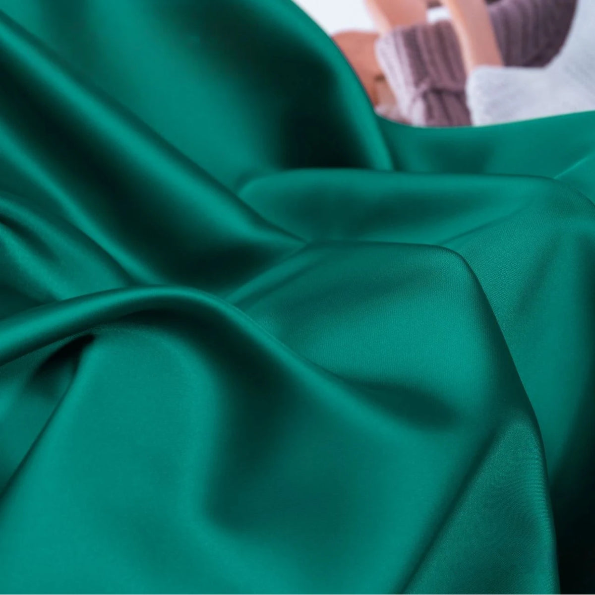 A close-up of Longan Craft’s Solid Color Charmeuse Satin Fabric by the yard shows its smooth, shiny thick bridal satin texture with soft folds; blurred in the background are parts of a casually dressed person.