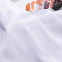 A white sheet partially covers plush toys, their socked feet peeking out—one is dressed in an outfit made from Longan Craft Solid Color Charmeuse Satin Fabric By The Yard, adding a touch of elegance to the scene.