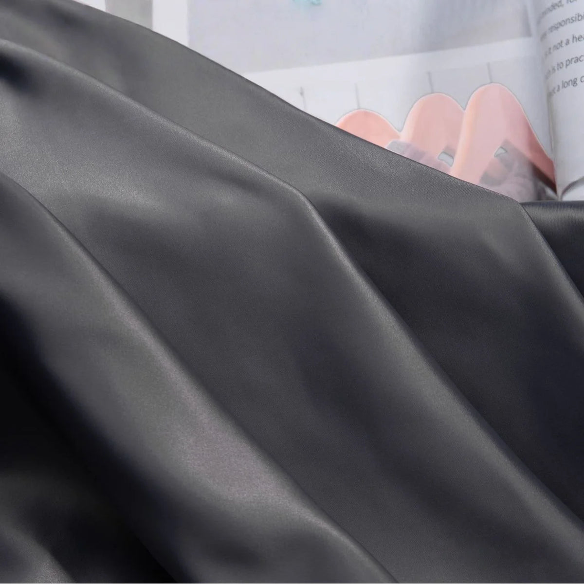 A close-up of Longan Craft Solid Color Charmeuse Satin Fabric By The Yard, featuring thick bridal satin texture in smooth folds, with an open magazine showing soft pink shapes in the background.