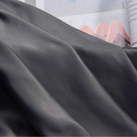 A close-up of Longan Craft Solid Color Charmeuse Satin Fabric By The Yard, featuring thick bridal satin texture in smooth folds, with an open magazine showing soft pink shapes in the background.