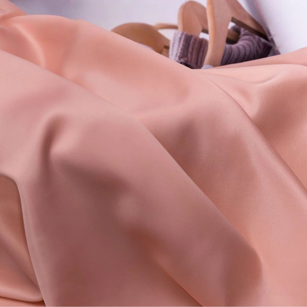 Soft peach Solid Color Charmeuse Satin Fabric by the yard from Longan Craft is draped with gentle folds, partially covering beige high-heeled sandals and a lilac ribbed garment in the background.