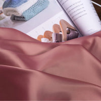 A close-up of Longan Craft’s Solid Color Charmeuse Satin Fabric By The Yard, featuring its thick, smooth satin texture for gowns, with a magazine beside it displaying folded knitwear and sweaters on wooden hangers.