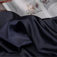 A close-up of Longan Craft Solid Color Charmeuse Satin Fabric By The Yard, featuring thick bridal satin with a smooth texture, draped in soft folds and an open magazine with photos and text in the background.