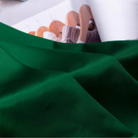 A close-up of Longan Craft's Solid Color Charmeuse Satin Fabric By The Yard, featuring thick bridal satin texture, is draped smoothly in the foreground; an open magazine with wooden hangers and knitted garments appears in the background.