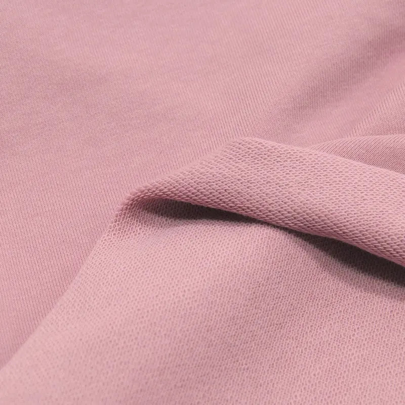 Close-up of Longan Craft's Solid Color Cotton French Terry Fabric By The Yard, showing its soft, light pink texture with a folded edge and both sides visible—ideal thick material for hoodies and other projects.