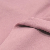 Close-up of Longan Craft's Solid Color Cotton French Terry Fabric By The Yard, showing its soft, light pink texture with a folded edge and both sides visible—ideal thick material for hoodies and other projects.