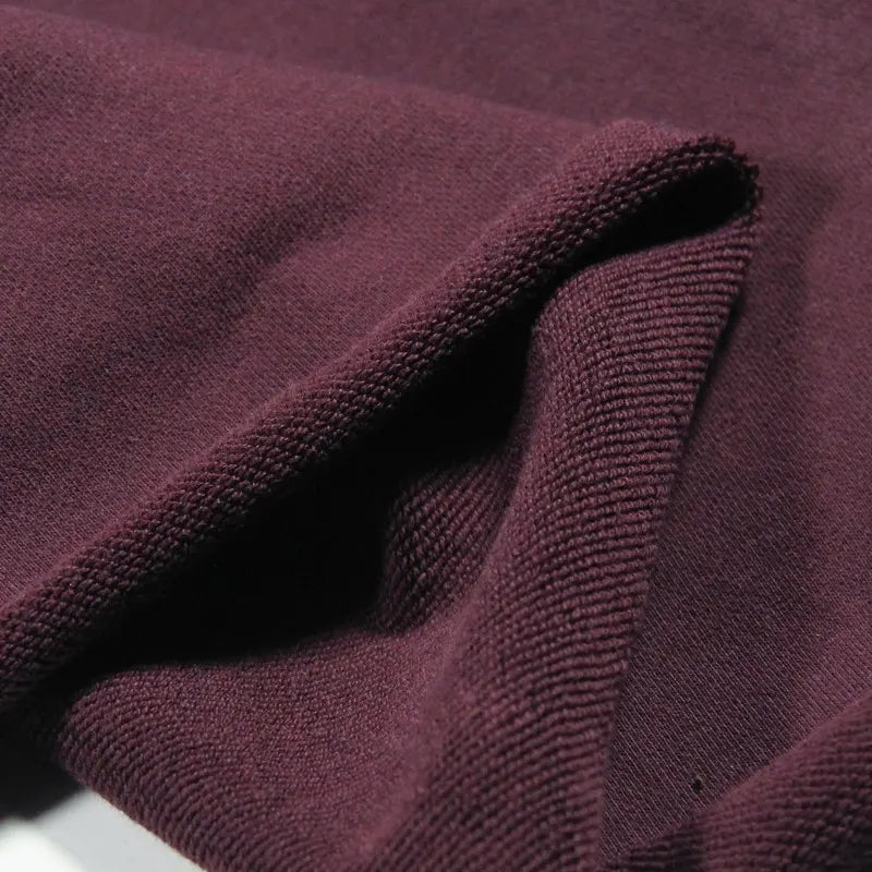A close-up of Longan Craft Solid Color Cotton French Terry Fabric by the yard in maroon, highlighting its thick, soft texture and folded edge—perfect material for hoodies.