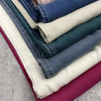 A stack of Solid Color Denim Lyocell Fabric by the yard from Longan Craft in cream, dark green, blue, and magenta with white edge stitching—wrinkle-free, breathable, and perfect for sustainable jeans and denim apparel.
