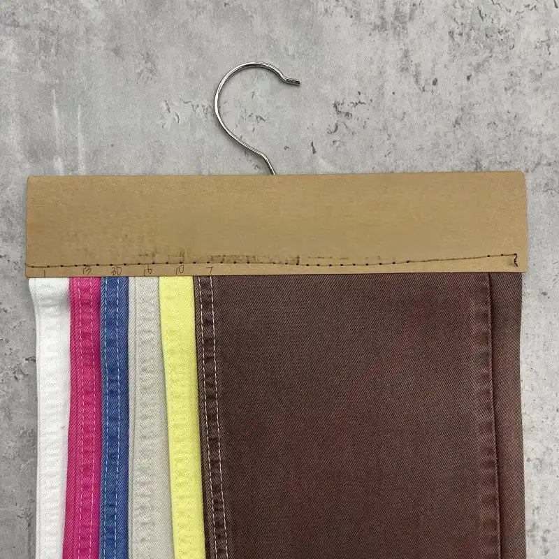 A hanger showcases Longan Craft's Solid Color Denim Lyocell Fabric swatches in five hues—white, pink, blue, yellow, and brown—neatly arranged on a gray background for sustainable fashion inspiration.