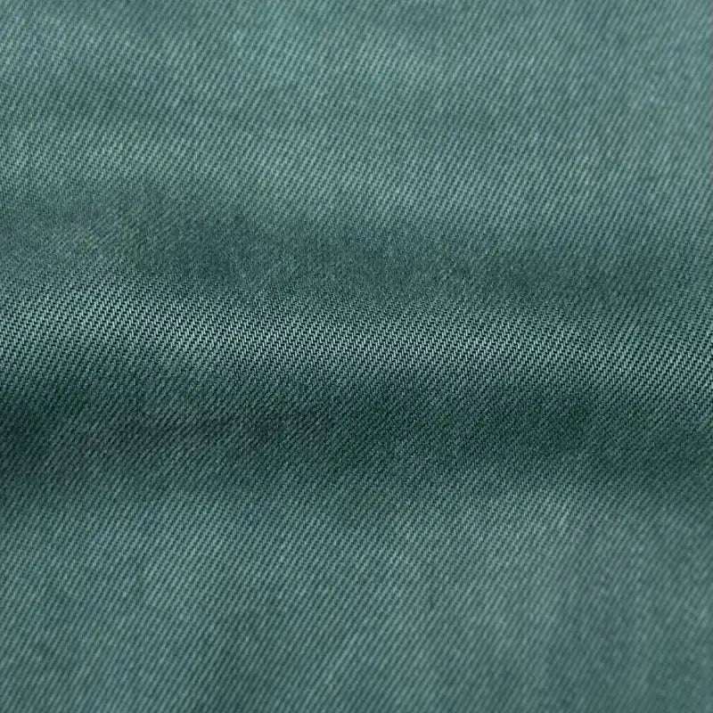 Close-up of Longan Craft’s Solid Color Denim Lyocell Fabric By The Yard, showing its green textured, diagonal weave and a horizontal crease. This wrinkle free, breathable lyocell textile is comfy and ideal for jeans.