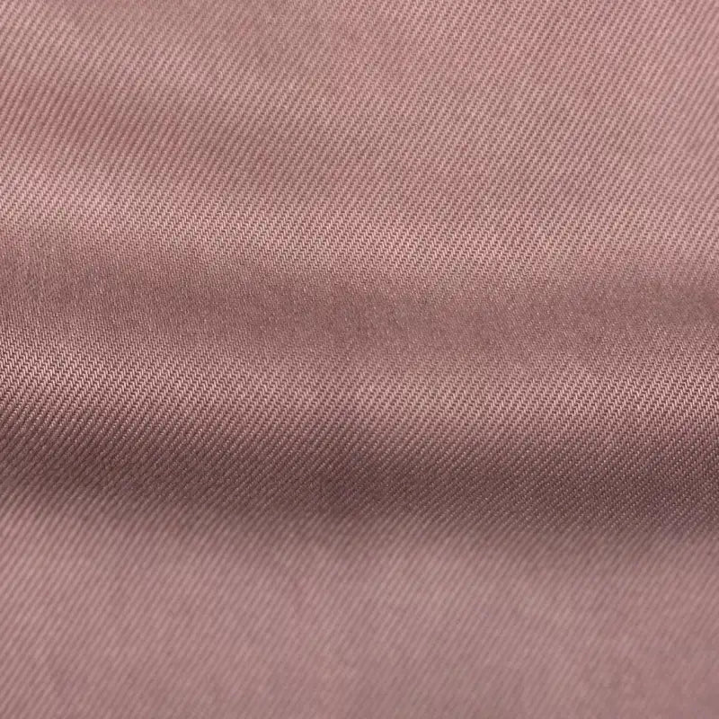 Close-up of Longan Craft’s Solid Color Denim Lyocell Fabric by the Yard, featuring a pinkish-brown hue, subtle diagonal weave, and gentle horizontal fold—this wrinkle-free, breathable, and comfy material is ideal for sustainable jeans.