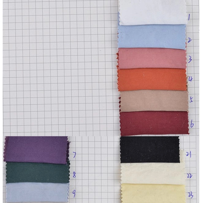 Nine rectangular swatches of Longan Craft’s Solid Color Double Sided Peachskin Fabric are arranged on grid paper, labeled 1–9 in blue. The microfiber polyester samples include shades like white, blue, red, brown, purple, black, green, and cream.