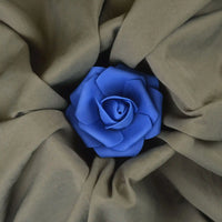 A vibrant blue artificial rose rests atop Longan Craft's Solid Color Double Sided Peachskin Fabric by the Yard, highlighting the soft brown microfiber polyester and its smooth, peachskin texture in a striking floral display.