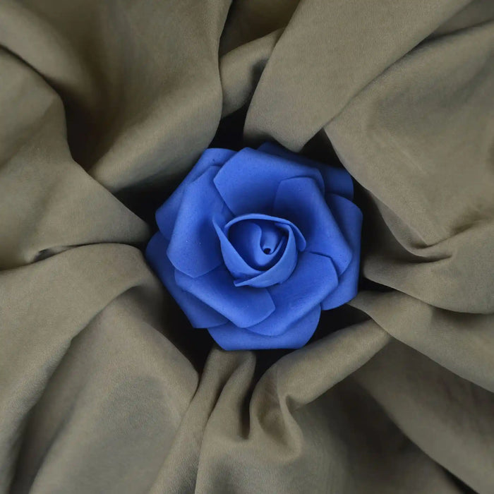 A vibrant blue artificial rose rests atop Longan Craft's Solid Color Double Sided Peachskin Fabric by the Yard, highlighting the soft brown microfiber polyester and its smooth, peachskin texture in a striking floral display.