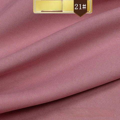 A close-up of Longan Craft’s Solid Color Linen Lyocell Fabric By The Yard reveals its soft, rose pink, smooth wrinkle-free twill texture. A gold and brown 21# label appears at the top. This sustainable fabric is gently folded.