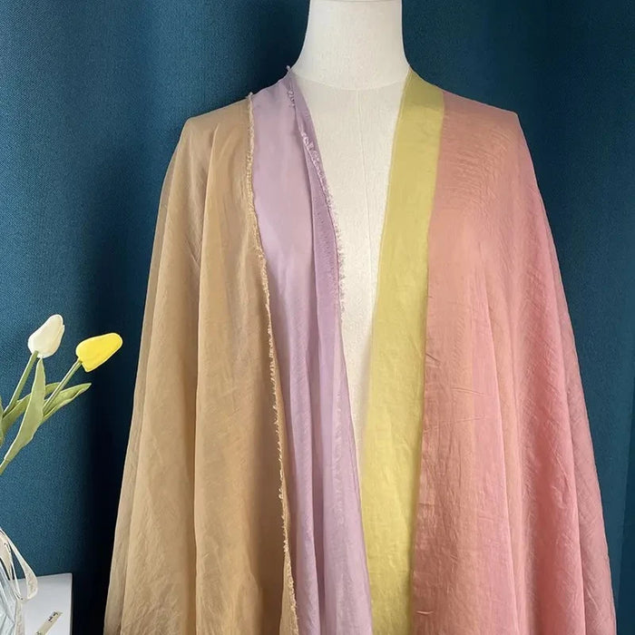 A mannequin displays Longan Craft’s Solid Color Linen Silk Fabric in beige, lavender, yellow, and pink against a blue background beside a vase of white and yellow tulips.