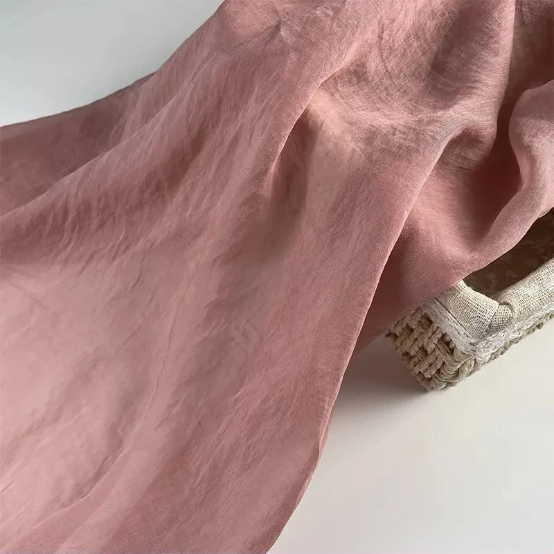 Longan Craft's Solid Color Linen Silk Fabric By The Yard, a soft thin lyocell silk blend in pink, is elegantly draped over a woven basket on a white surface—ideal as perfect silk upholstery fabric.