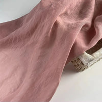 Longan Craft's Solid Color Linen Silk Fabric By The Yard, a soft thin lyocell silk blend in pink, is elegantly draped over a woven basket on a white surface—ideal as perfect silk upholstery fabric.