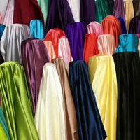 Longan Craft’s Solid Color Polyester Satin Fabric by the yard, with a silky stretch texture in vibrant shades like red, purple, blue, green, yellow, orange, and cream, is neatly displayed upright in a fabric store—ideal for blouses.