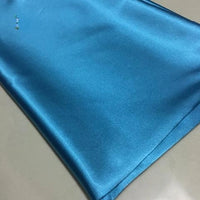 A neatly folded piece of Longan Craft Solid Color Polyester Satin Fabric in shiny light blue rests on a smooth, light-colored surface—perfect silky stretch satin material for blouses, available by the yard.