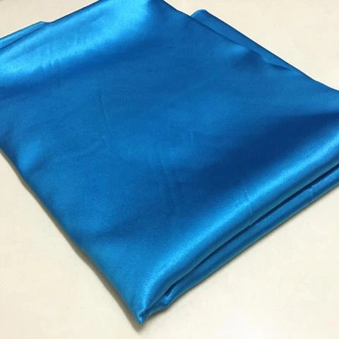 A folded piece of turquoise blue Longan Craft Solid Color Polyester Satin Fabric with a silky stretch texture rests on a light surface—ideal satin material for blouses.