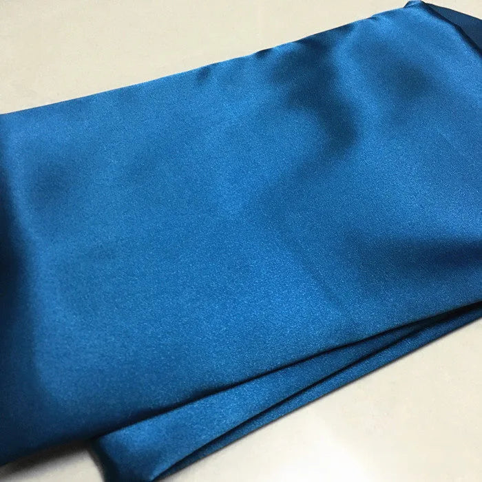 A piece of Longan Craft Solid Color Polyester Satin Fabric, featuring a silky stretch satin texture in blue, is displayed on a light surface—ideal material for blouses by the yard.