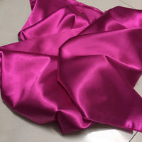 Longan Craft's Solid Color Polyester Satin Fabric By The Yard in bright pink is displayed slightly crumpled on a light surface, highlighting its silky stretch satin texture—ideal material for blouses.