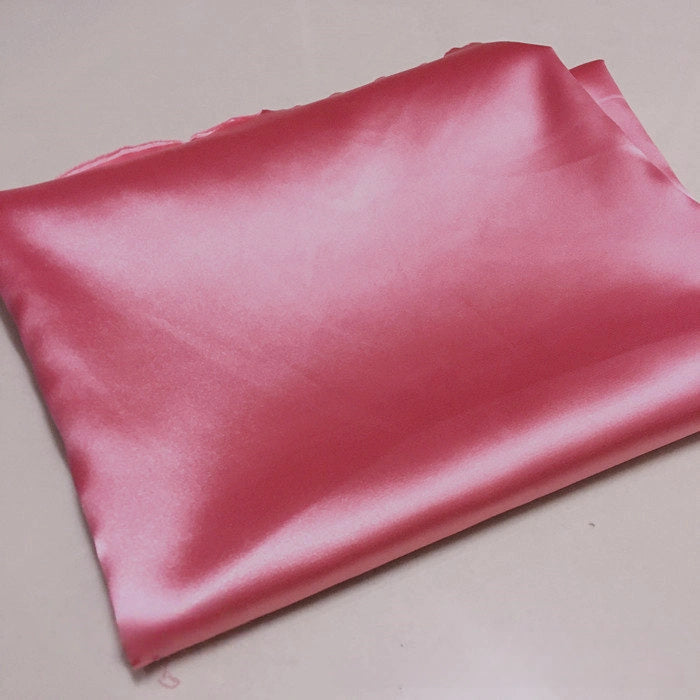 A piece of Longan Craft Solid Color Polyester Satin Fabric in pink, featuring a silky stretch satin texture, rests on a smooth light surface—ideal material for blouses by the yard.
