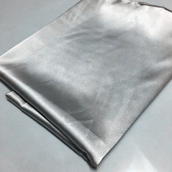 A folded piece of Longan Craft Solid Color Polyester Satin Fabric By The Yard rests on a light grey surface, showcasing its silky stretch satin texture and smooth, reflective finish—ideal material for blouses.