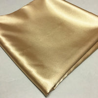 A piece of Longan Craft Solid Color Polyester Satin Fabric By The Yard in shiny gold is shown on a white surface. This silky stretch satin material is smooth and glossy—ideal for blouses.