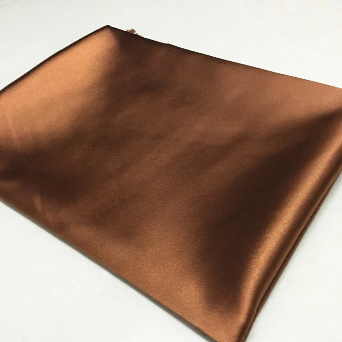 A piece of Longan Craft Solid Color Polyester Satin Fabric by the yard, featuring a silky stretch satin texture in rich brown, is folded and laid flat on a light surface—perfect for blouses.