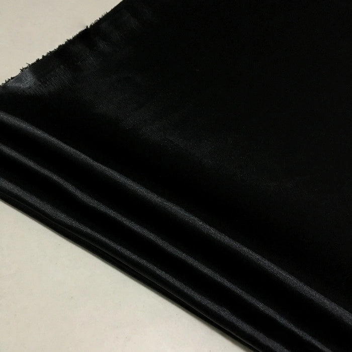 A folded piece of Longan Craft Solid Color Polyester Satin Fabric By The Yard lies on a light surface, showcasing its silky stretch satin texture and lustrous sheen—ideal for blouses.