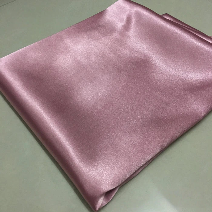A piece of Longan Craft Solid Color Polyester Satin Fabric By The Yard in pink, featuring a silky stretch satin texture, rests on a light surface—perfect material for blouses.