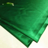 A piece of green Solid Color Polyester Satin Fabric by Longan Craft, with silky stretch satin texture and a lighter spot near the top left corner, lies on a white surface.