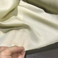 A hand holding the edge of Longan Craft’s Solid Color Ramie Fabric By The Yard, a super lightweight lyocell-ramie material with visible stitching along the hem, showcases its light color and breathable, semi-transparent texture against a neutral background—ideal for blouses.