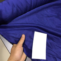 A hand holds a piece of Solid Color Ramie Fabric By The Yard from Longan Craft—the super lightweight Lyocell ramie material in vibrant blue—while a plain white rectangular card placed on top highlights the fabric’s color and breathable texture, ideal for blouses.