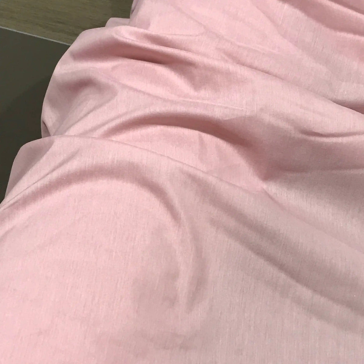 A close-up view of the Longan Craft Solid Color Ramie Fabric By The Yard in a soft, light pink shade, showcasing its gentle folds and creases. This super lightweight lyocell ramie material lies flat, highlighting its breathable texture—ideal for making blouses.