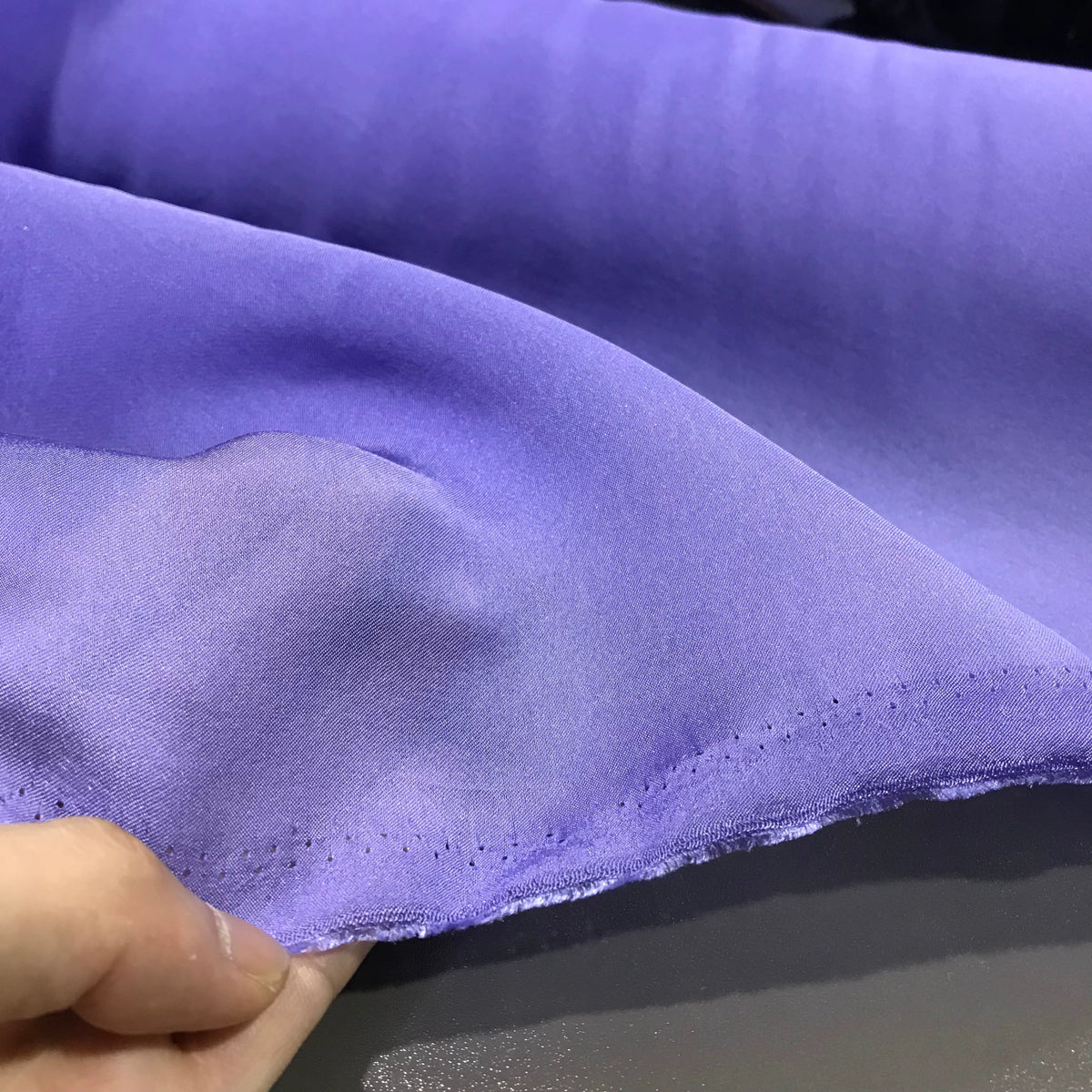 A close-up of a hand holding the edge of Longan Craft’s Solid Color Ramie Fabric By The Yard showcases its super lightweight lyocell ramie material in light purple, with visible hem stitching and highlighting its breathable qualities—ideal for blouses.