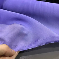 A close-up of a hand holding the edge of Longan Craft’s Solid Color Ramie Fabric By The Yard showcases its super lightweight lyocell ramie material in light purple, with visible hem stitching and highlighting its breathable qualities—ideal for blouses.