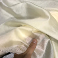 A close-up of a hand holding a piece of Longan Craft’s Solid Color Ramie Fabric By The Yard, showcasing the super lightweight lyocell ramie material in a light cream shade, with its smooth, slightly shiny texture and breathable, semi-translucent quality—ideal for making blouses.