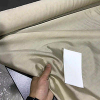 A hand holds a roll of Longan Craft’s Solid Color Ramie Fabric By The Yard—a super lightweight lyocell ramie material—that is spread across a dark surface. A small white rectangular paper rests on the breathable fabric, ideal for blouses.