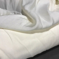 A close-up of Longan Craft’s Solid Color Ramie Fabric by the yard showcases its super lightweight lyocell ramie material in white, with gentle folds and creases laying flat. The breathable fabric appears smooth and slightly sheer, catching light and casting subtle shadows—ideal for blouses.
