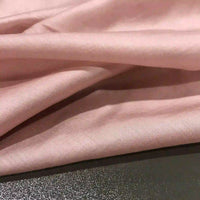 Super lightweight lyocell ramie fabric by Longan Craft in a soft, light pink solid color, elegantly draped in gentle folds across a textured dark surface—perfect breathable material for blouses.