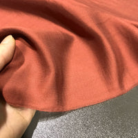 A hand gently pinches the edge of Longan Craft’s Solid Color Ramie Fabric by the Yard, a super lightweight lyocell ramie material, highlighting its soft texture, breathable quality, and subtle sheen against a gray surface—perfect for blouses.