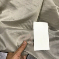 A hand holds a piece of Longan Craft Solid Color Ramie Fabric by the yard—super lightweight lyocell ramie material—while comparing it to a small rectangular white color sample.