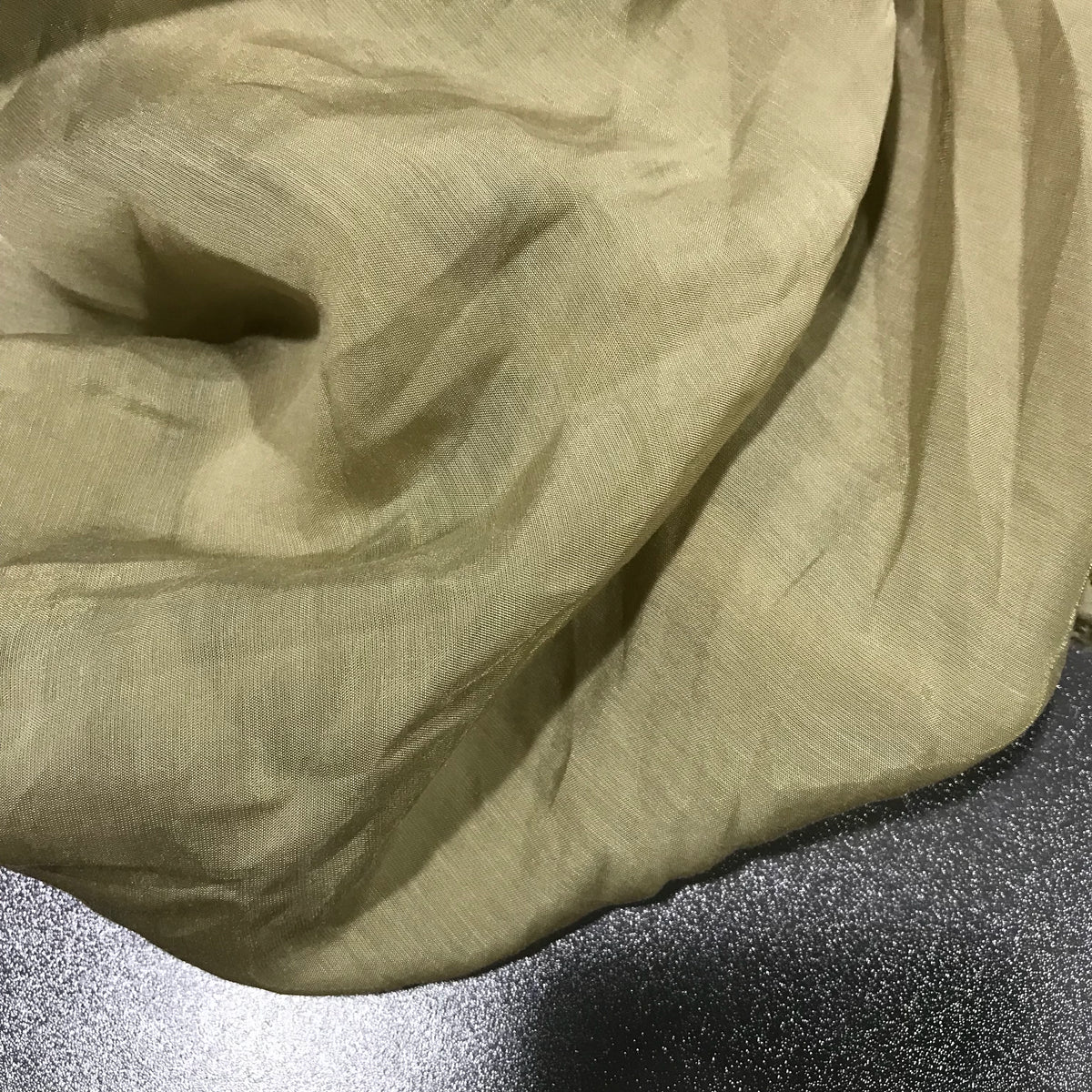 A close-up of Longan Craft’s Solid Color Ramie Fabric By The Yard—a super lightweight, breathable lyocell ramie material in light beige—displaying its soft folds as it rests on a dark, textured surface.